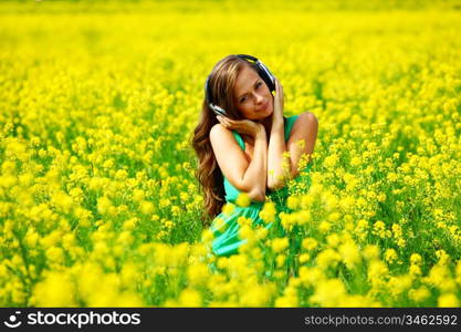 Young woman with headphones listening to music on oilseed flowering field