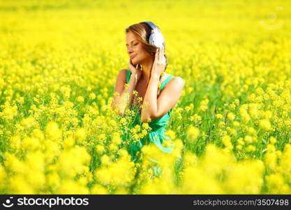 Young woman with headphones listening to music on oilseed flowering field