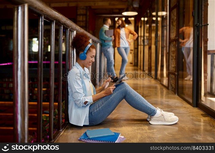 Young woman with headphones sitting on floor and using digital tablet in coworking office. Young woman with headphones sitting on floor and using digital tablet