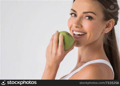 Young woman with healthy teeth smiling and biting green apple. Woman biting green apple