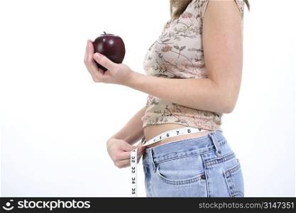 Young woman with holding measuring tape around waist and an apple.