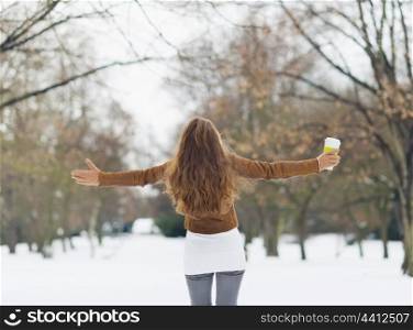 Young woman with hot beverage in winter park. Rear view