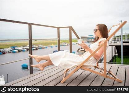 Young woman with hot coffee enjoying view of lake. Beautiful woman relax during exotic vacation on the beach enjoying sweet coffee. Young woman drinking hot coffee enjoying beach view.