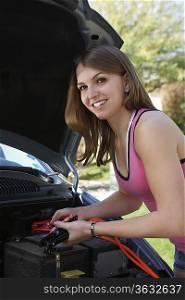 Young woman with jumper cables by car