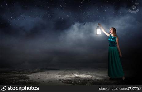 Young woman with lantern walking in darkness. Lost in darkness