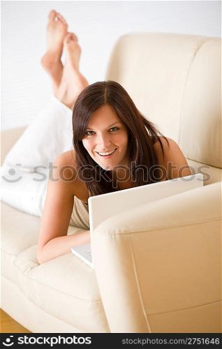 Young woman with laptop lying down on sofa home in living room