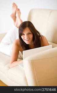 Young woman with laptop lying down on sofa home in living room