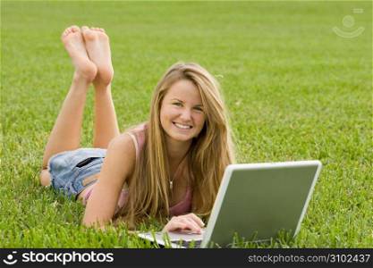 Young woman with laptop lying in lawn, portrait