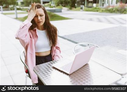 Young woman with laptop with facepalm gesture, feeling regret, sorrow, blaming herself for mistake, raise her hand, sitting in street cafe. Freelance, online business, online work. Copy space. Young woman with laptop with facepalm gesture, feeling regret, sorrow, blaming herself for mistake