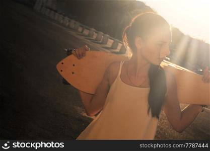 Young Woman with longboard behind her neck backlit by bright summer sun a lot of space for text. Young Woman with longboard behind her neck backlit by bright summer sun