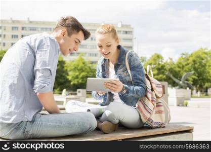 Young woman with male friend using digital tablet at college campus