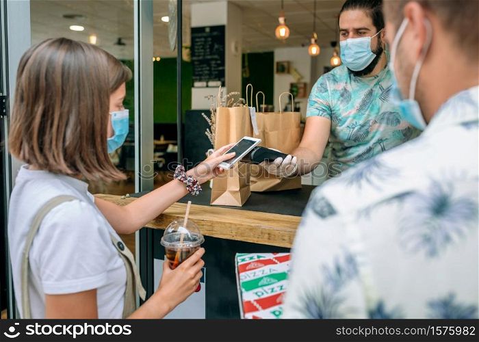 Young woman with mask paying with mobile a take away order. Woman paying with mobile a take away order