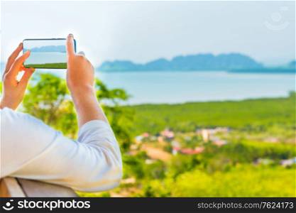 Young woman with mobile phone taking image of Thailand mountain island sea landscape