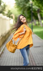 Young woman with moving hair wearing casual clothes and modern bag in urban background. Happy girl with wavy hairstyle in the wind.