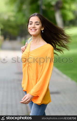 Young woman with moving hair wearing casual clothes in urban background. Happy girl with wavy hairstyle in the wind.