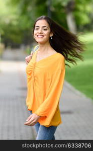 Young woman with moving hair wearing casual clothes in urban background. Happy girl with wavy hairstyle in the wind.