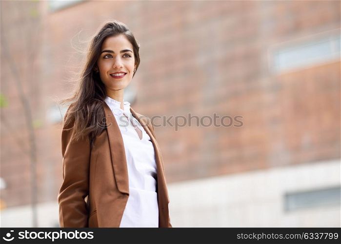 Young woman with nice hair standing outside of office building. Businesswoman wearing formal wear with wavy hairstyle. Young girl with brown jacket and trousers.
