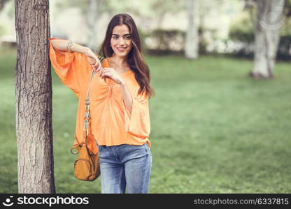 Young woman with nice hair wearing casual clothes and bag in urban background. Happy girl with wavy hairstyle in a park in the city.