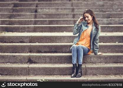 Young woman with nice hair wearing casual clothes in urban background. Happy girl with wavy hairstyle sitting in urban stairs.