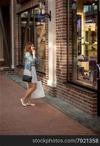 Young woman with paper bag looking at store window