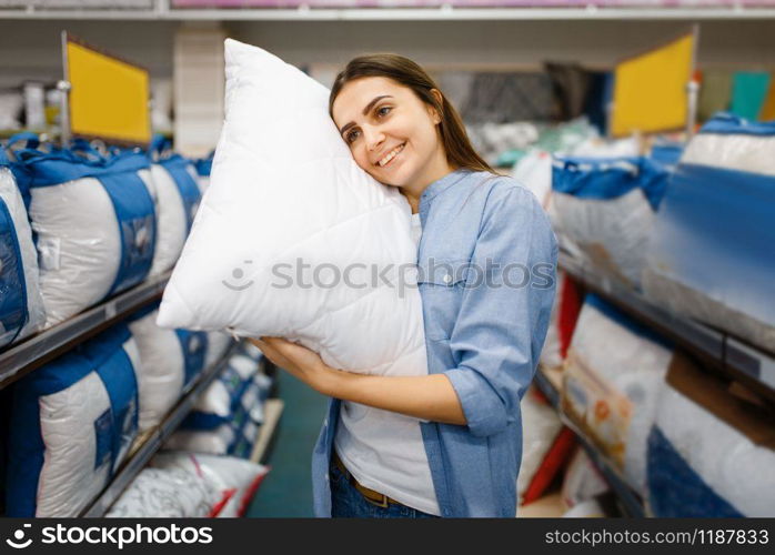 Young woman with pillows in bed linen store. Female person buying home goods in market, lady in bedding shop. Young woman with pillows in bed linen store