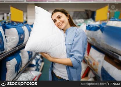 Young woman with pillows in bed linen store. Female person buying home goods in market, lady in bedding shop. Young woman with pillows in bed linen store