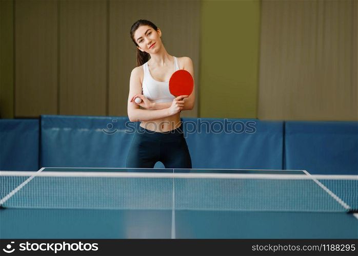 Young woman with ping pong racket and ball at the table indoors. Female person in sportswear, training in table-tennis club. Young woman with ping pong racket at the table