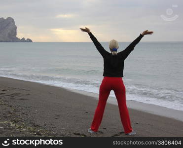 Young woman with raised hands standing on sand and looking to a sky