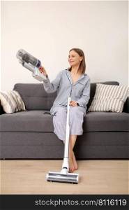 Young woman with rechargeable vacuum cleaner sitting on sofa and at home. girl tries to fold the vacuum cleaner according to the instructions.. Young woman with rechargeable vacuum cleaner sitting on sofa and at home. girl tries to fold the vacuum cleaner according to the instructions