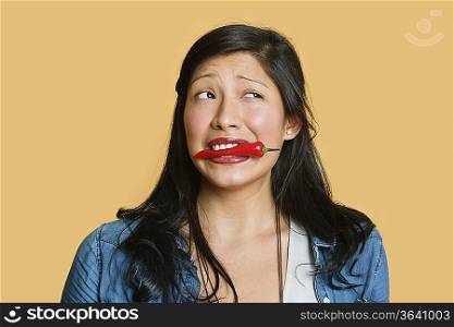 Young woman with red chili pepper in mouth over colored background