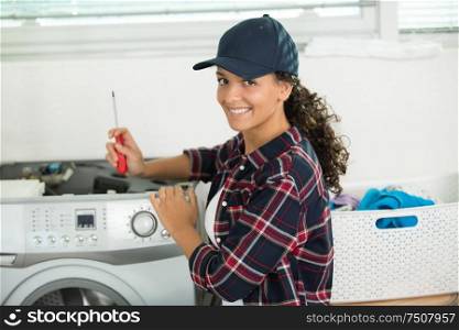 young woman with screwdriver repairing washing machine