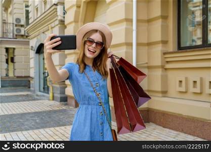 Young Woman with shopping bags making selfie walking in a city at summer day.. Young Woman with shopping bags making selfie walking in a city at summer day