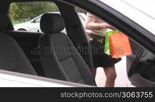 Young woman with shopping bags turning car on