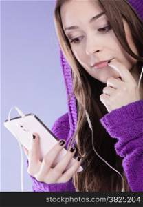 young woman with smart phone listening music. Teen stylish long hair girl in hood relaxing or learning language. Studio shot on violet.