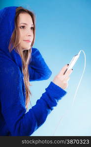 young woman with smart phone listening music. Teen stylish long hair girl in hood relaxing or learning language Studio shot on blue.