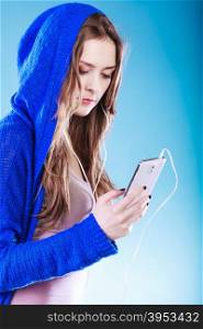 young woman with smart phone listening music. Teen stylish long hair girl in hood relaxing or learning language. Studio shot on gray.