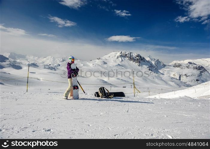 Young woman with snowboard in ski goggles outdoors with French Alps covered with snow at background. Val-d'Isere, France