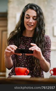 Young woman with some gray hair taking a photograph with her smartphone in a cafe bar.. Young woman with some gray hair using smartphone in a cafe.