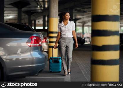 Young woman with suitcase in car parking. Female traveler with luggage in vehicle park lot, passenger with bag. Girl with baggage. Young woman with suitcase in car parking