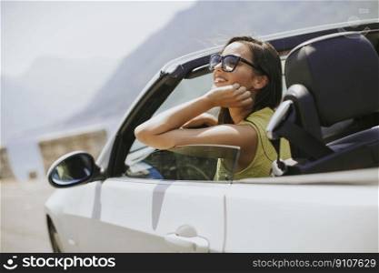 Young woman with sunglasses driving her convertible top automobile on bright sunny day near sea
