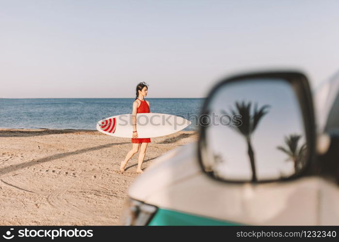 Young woman with surfboard on the beach near a van