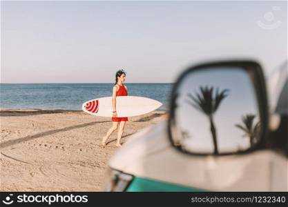 Young woman with surfboard on the beach near a van