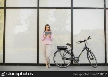 Young woman with tablet and e-bike outdoor on sunny day