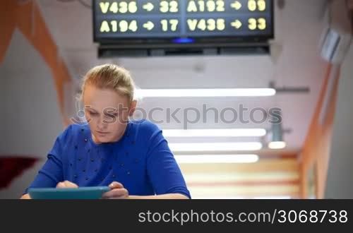 Young woman with touchpad in the waiting room of the airport. Display board in the background