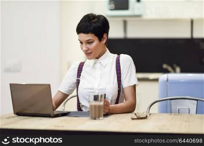 Young woman with very short haircut typing with a laptop at home. Businesswoman working at home concept.