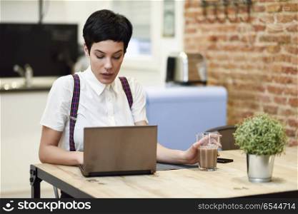 Young woman with very short haircut typing with a laptop at home. Young woman with very short haircut typing with a laptop at home. Businesswoman working at home concept.