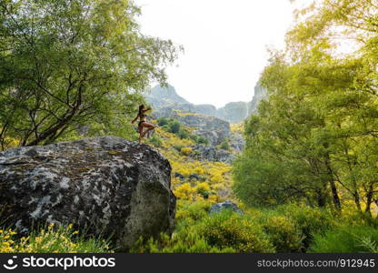 Young woman woman practices balance yoga asana tree pose on a sunny bright day. Incredibly beautiful landscape. On background forest.