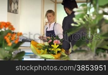 Young woman working as florist giving receipt and credit card to customer after purchase. Dolly shot