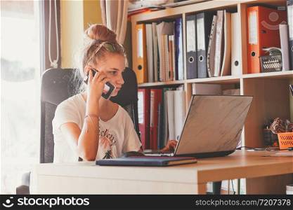 Young woman working at home, using portable computer, sitting at desk in home office. Candid people, real moments, authentic situations