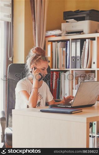Young woman working at home, using portable computer, sitting at desk in home office. Candid people, real moments, authentic situations